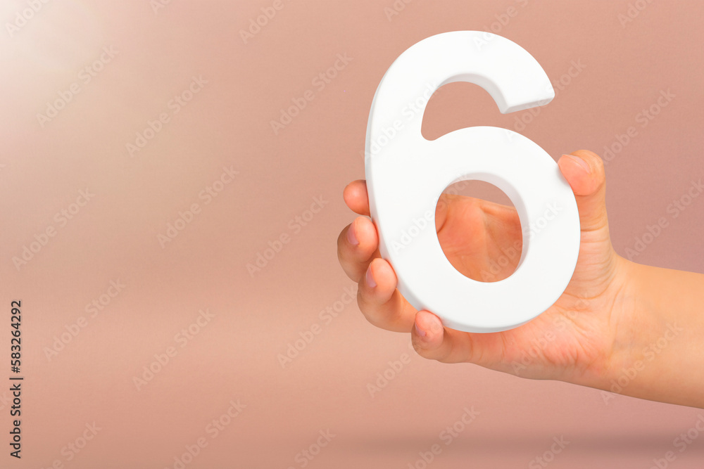 Number six in hand. A hand holds a white number 6 on a red background with copy space. Concept ...