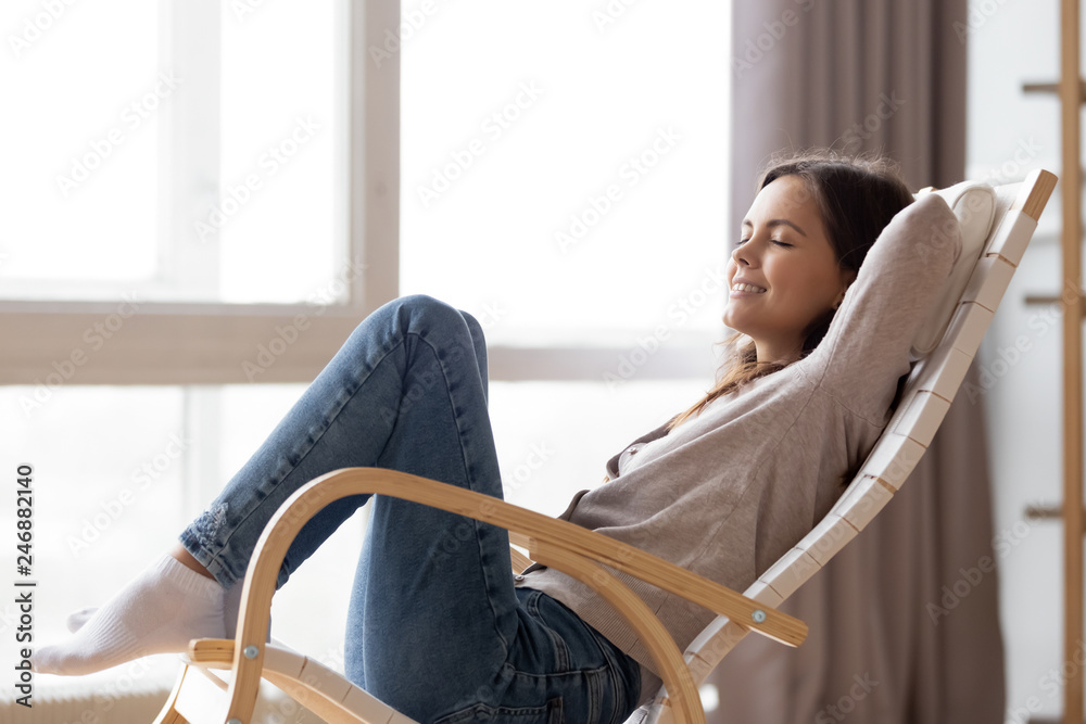 Relaxed Calm Young Woman Lounging Sitting In Comfortable Wooden Rocking Chair Breathing Fresh...