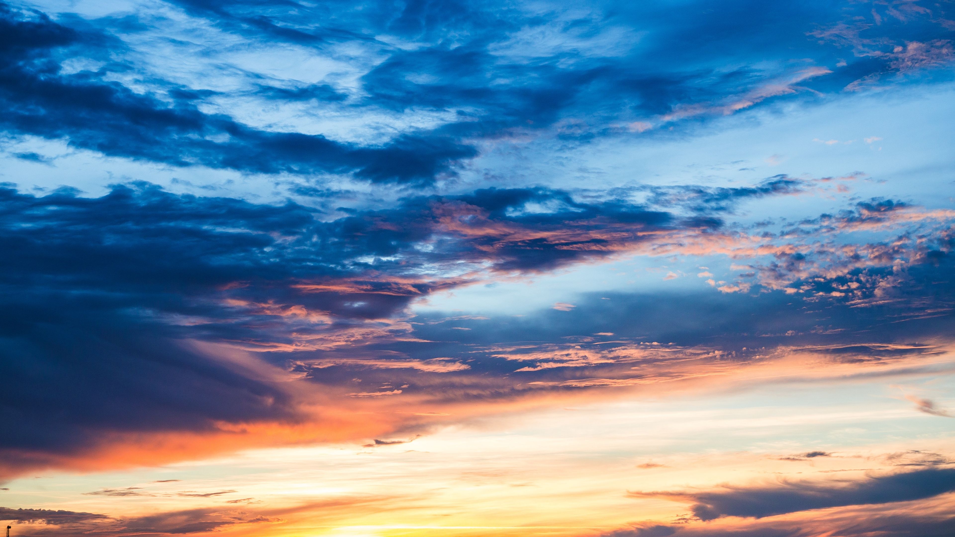 The Sun Is Setting Behind Some Clouds In The Blue And Orange Sky With White Fluffy Clouds